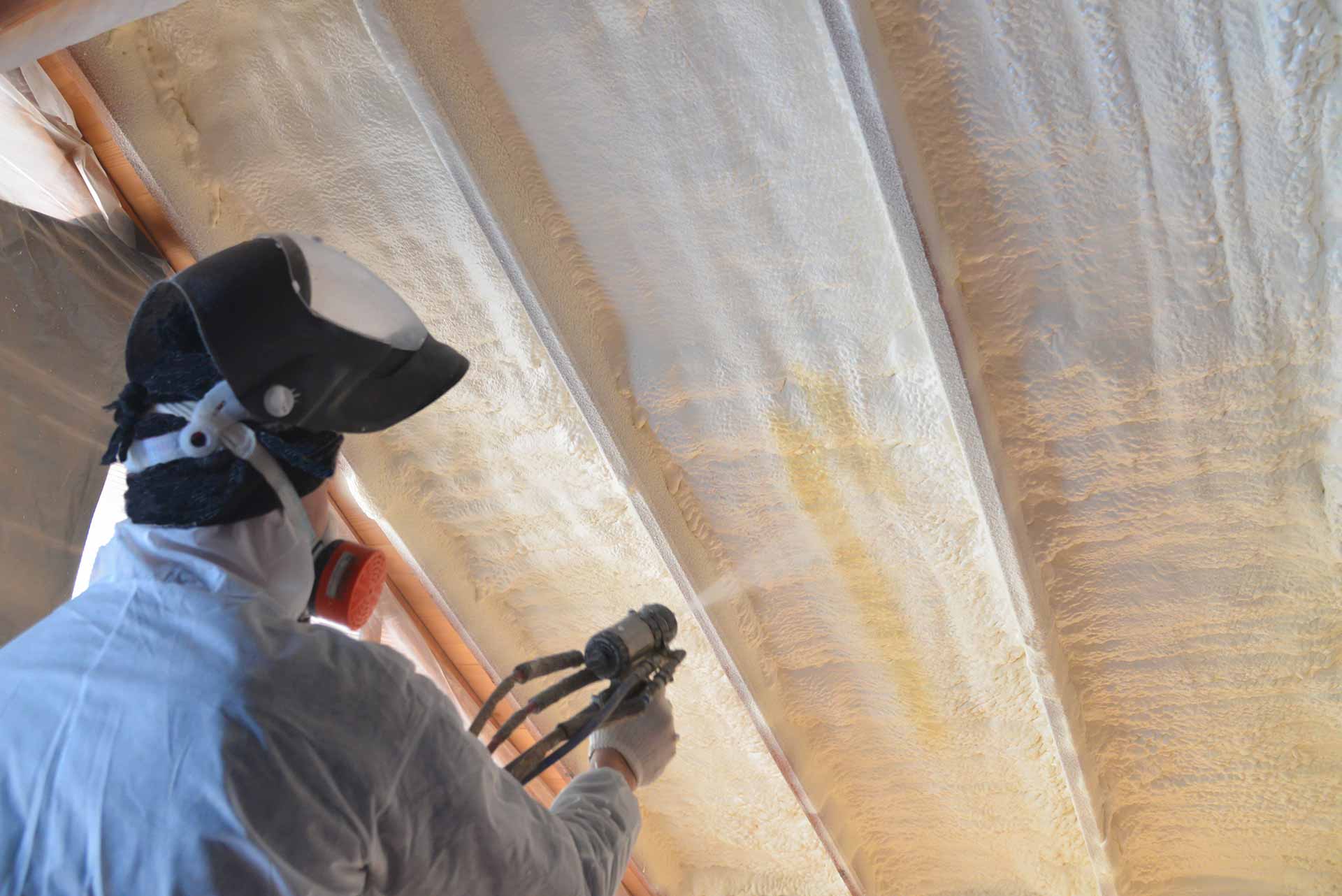 Worker spraying foam insulation in attic
